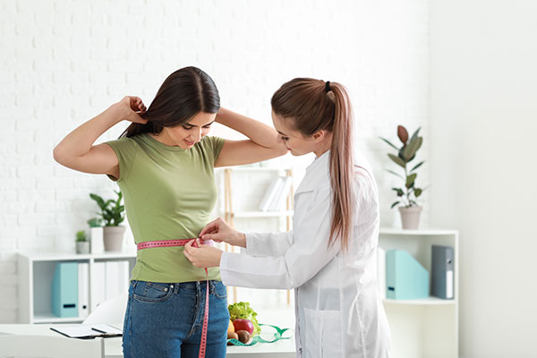 A doctor measures a patient's waist with a tape measure.